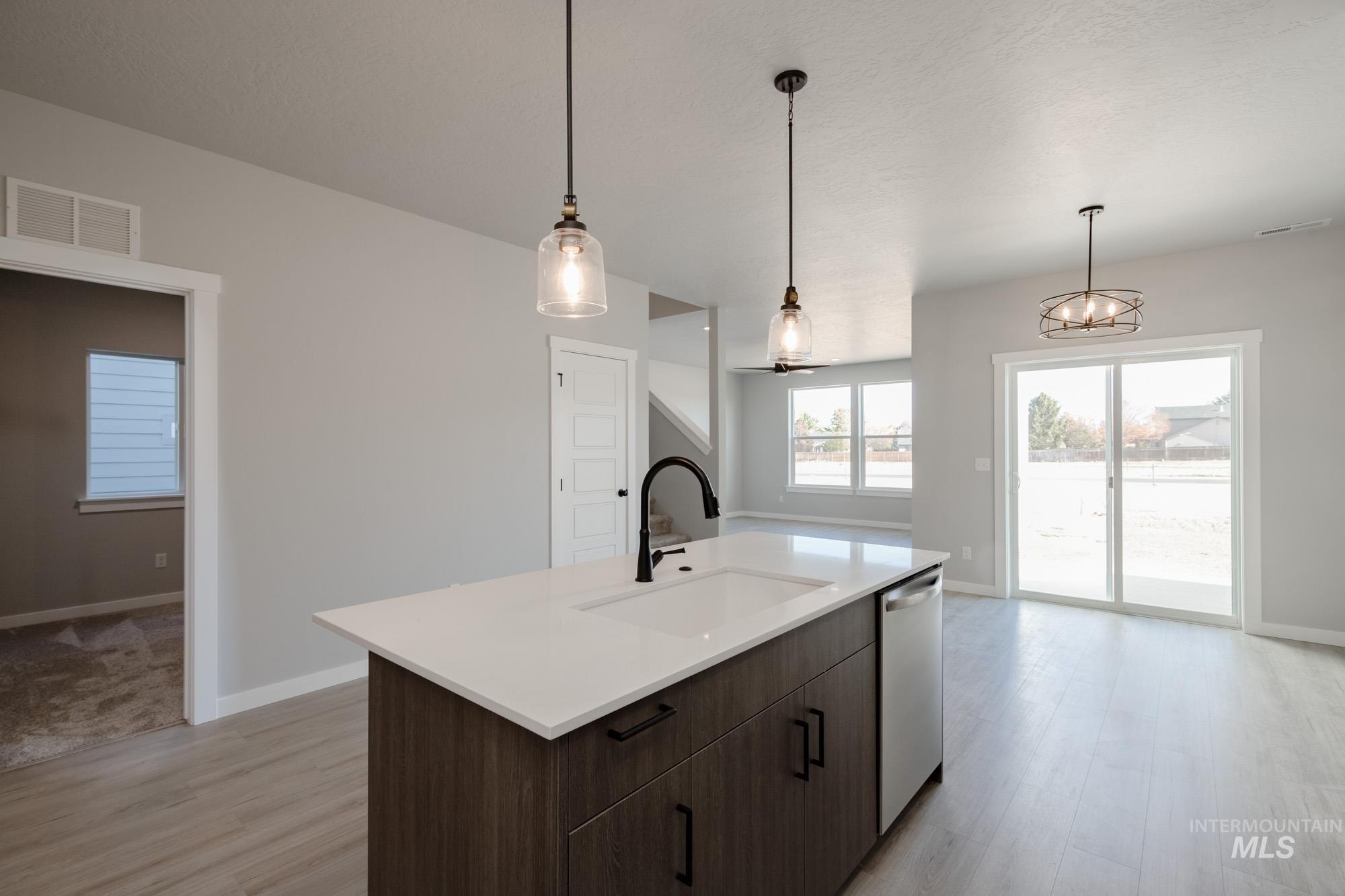 2058 South Border Way Meridian, ID 83642 - Photo 7 of 25 Kitchen featuring dark wood finish cabinetry, light wood-type flooring, a center island with sink, dishwasher, and hanging lights