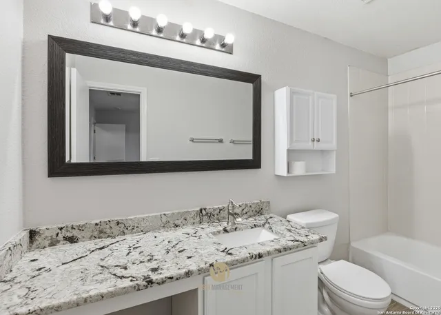 a bathroom with a granite countertop sink a toilet and mirror