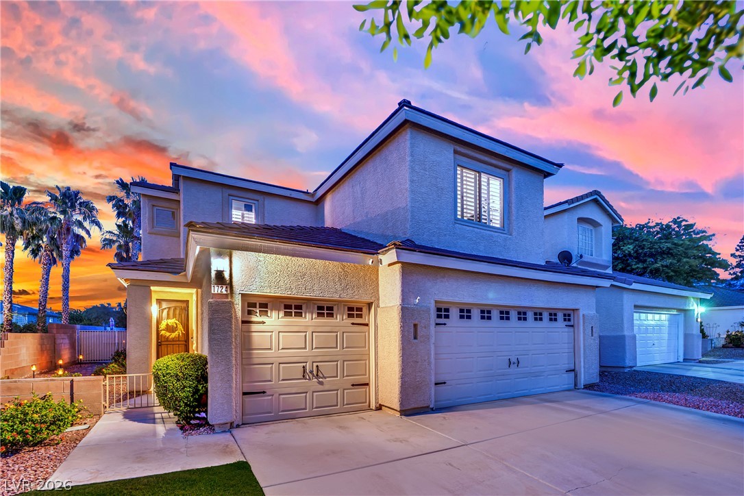 1724 Millstream Way Henderson, NV 89074 - Photo 46 of 60 A striking stucco facade greets you, featuring multiple garage doors and a welcoming entryway under a vibrant sunset.