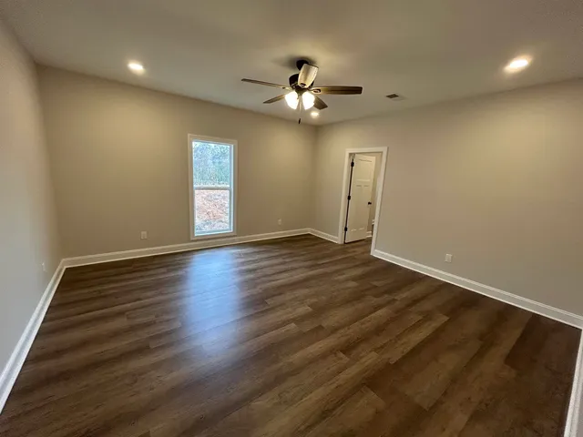 an empty room with wooden floor chandelier fan and windows