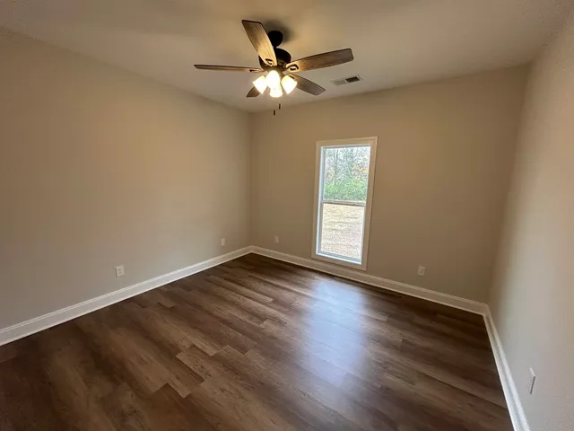 an empty room with wooden floor chandelier fan and windows