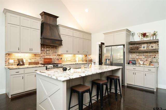 2151 Byrd Road Jacksonville, TX 75766 - Photo 9 of 40 Kitchen featuring decorative backsplash, vaulted ceiling, a breakfast bar, light stone countertops, and a kitchen island with sink