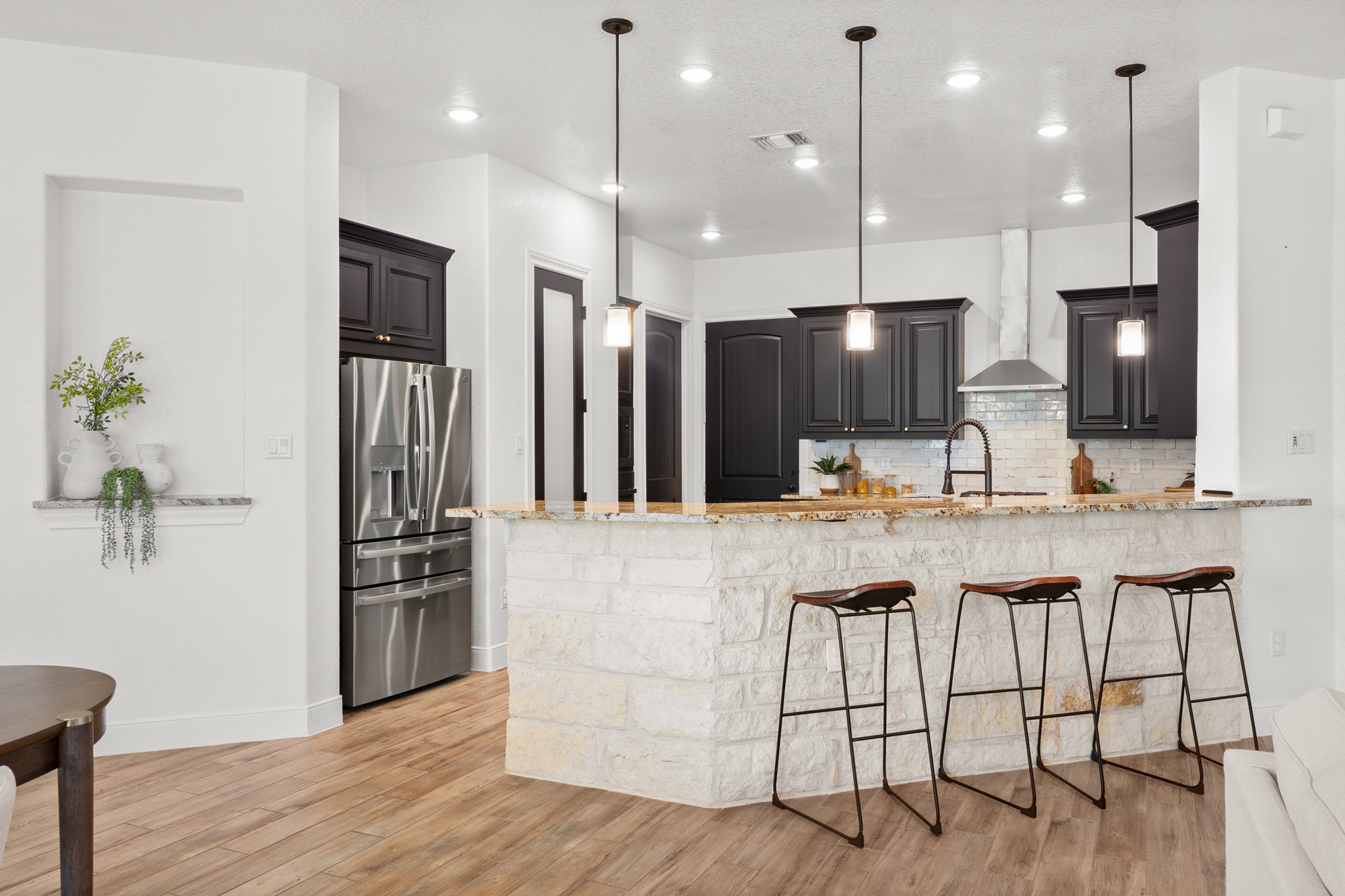 128 Hiram Cook Blanco, TX 78606 - Photo 7 of 40 Open-concept kitchen featuring dark cabinetry, stainless steel appliances, a stone-clad island with a granite countertop, pendant lighting, and wood-finish flooring