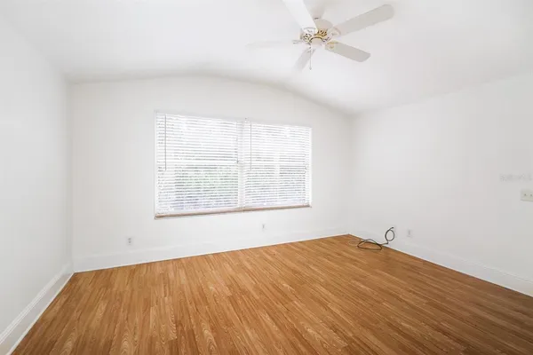 an empty room with wooden floor ceiling fan and windows
