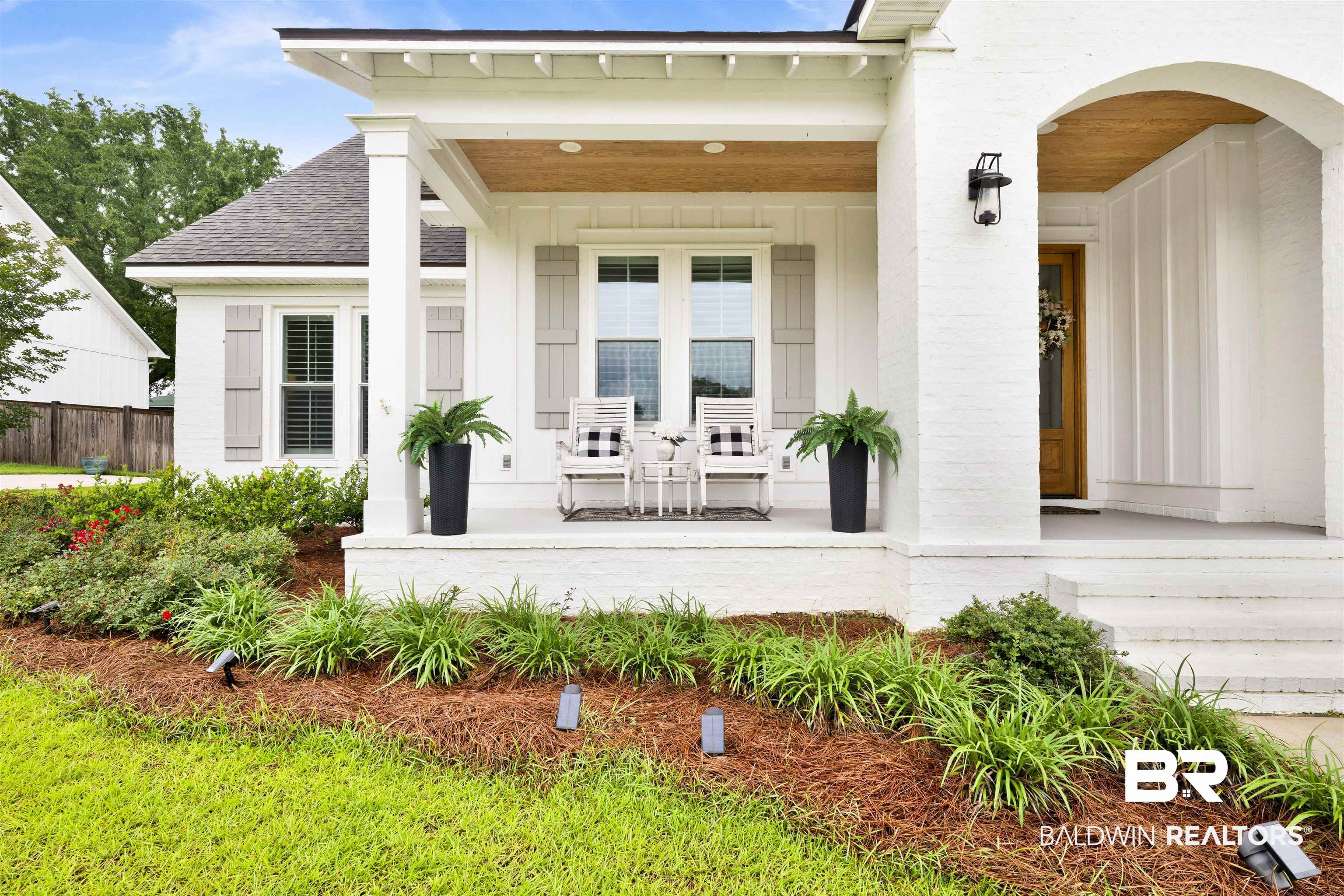 21702 Pillars Street Fairhope, AL 36532 - Photo 2 of 54 Inviting front porch featuring a wood-finish ceiling, white brick and siding exterior, grey louvered shutters, and established landscaping with ground lighting