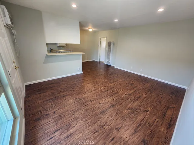 an empty room with wooden floor and a kitchen