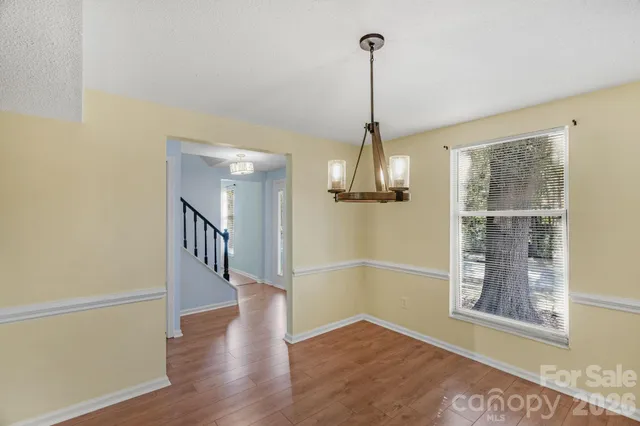 a view of an empty room with wooden floor kitchen view and a window