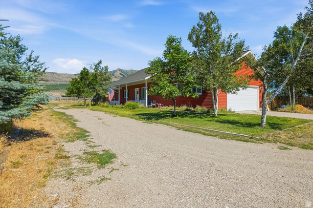 1634 West Arimo Road Arimo, ID 83214 - Photo 88 of 89 Red siding residence with an attached garage, a covered porch, a gravel driveway, and surrounding mature trees