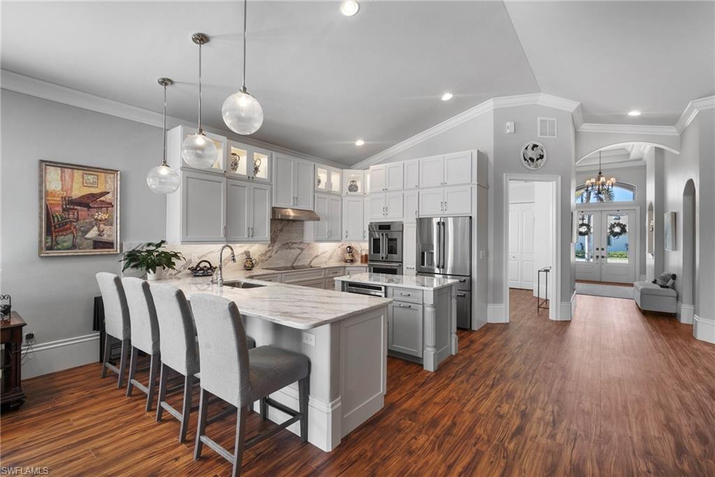 10340 Vanderbilt Drive Naples, FL 34108 - Photo 18 of 45 a large kitchen with stainless steel appliances kitchen island granite countertop a stove a refrigerator a oven a dining table and chairs with wooden floor