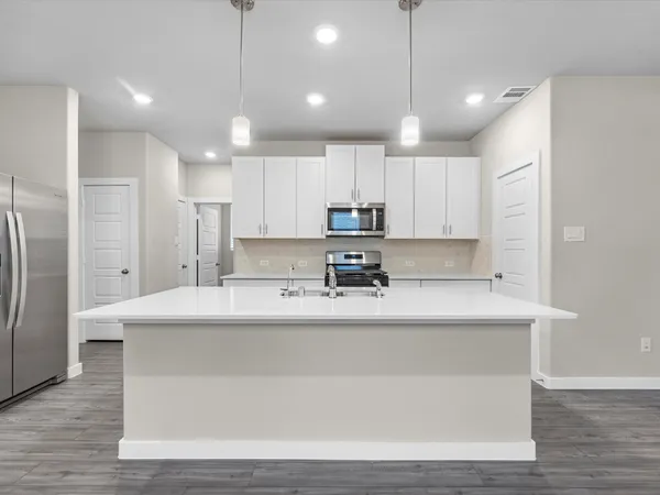 a large white kitchen with kitchen island a sink a center island stainless steel appliances and a refrigerator