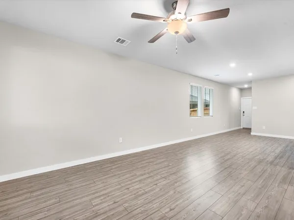 an empty room with wooden floor fan and windows
