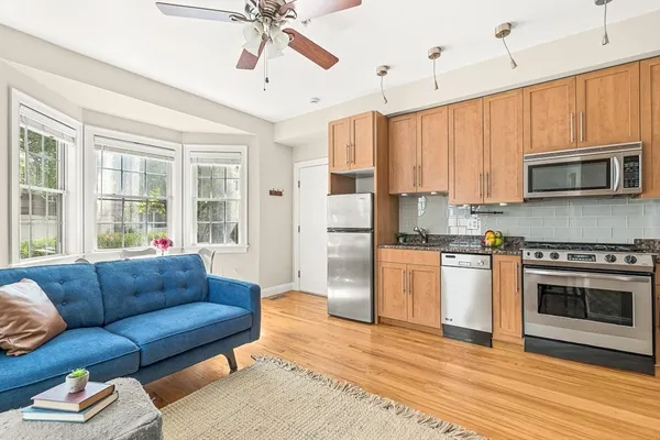a living room with stainless steel appliances granite countertop a fireplace a flat screen tv a stove and a window