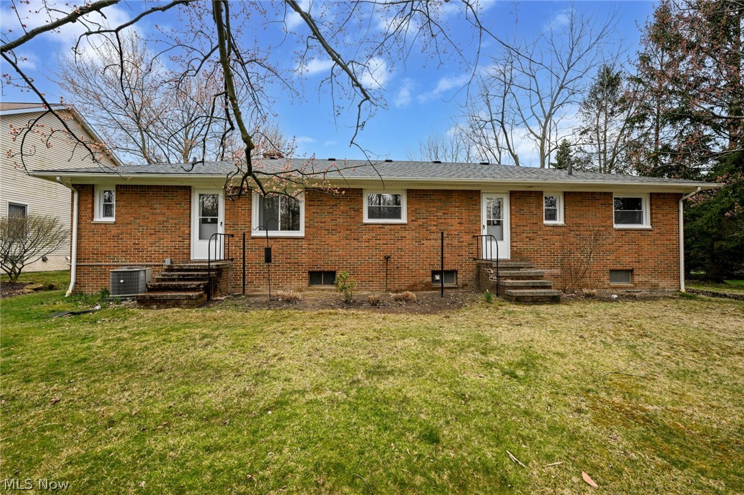 Rear view of house featuring central AC unit and a lawn