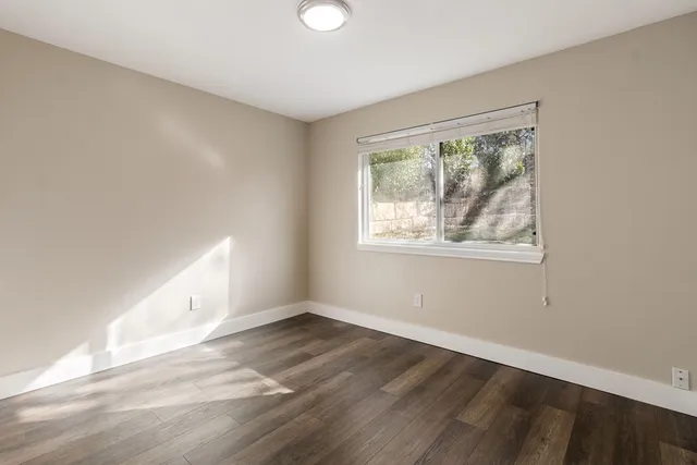 a view of an empty room with wooden floor and a window