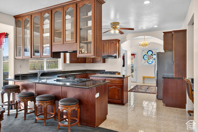 4768 East Hickman Canyon Road Stockton, UT 84071 - Photo 15 of 85 Kitchen with a peninsula, arched walkways, dark stone counters, stainless steel fridge, and light tile patterned floors.