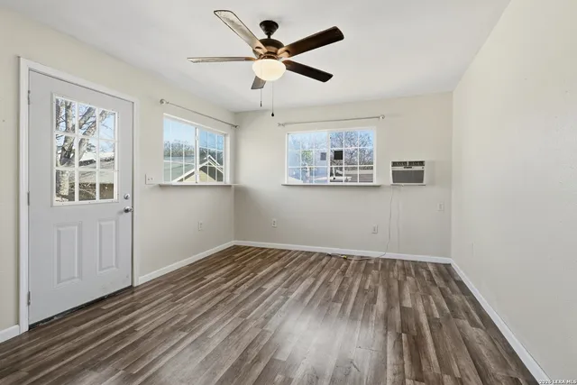 an empty room with wooden floor chandelier fan and windows