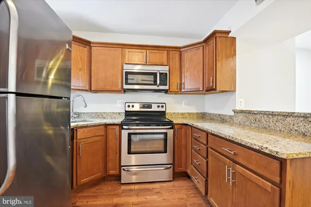 a kitchen with stainless steel appliances granite countertop wooden cabinets a stove a sink and dishwasher with wooden floor