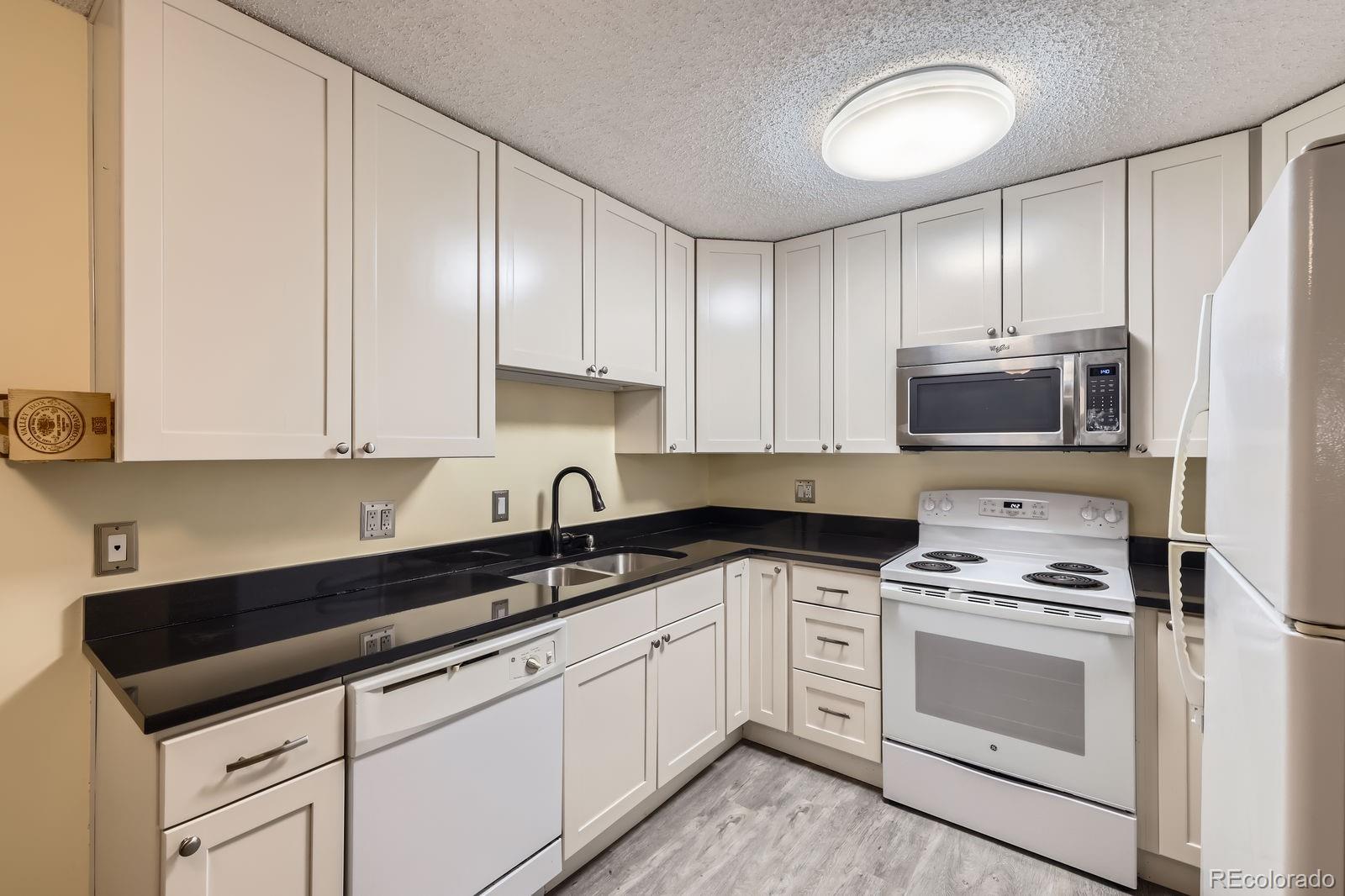 3124 South Wheeling Way, Unit 102 Aurora, CO 80014 - Photo 10 of 17 a kitchen with granite countertop white cabinets and white appliances