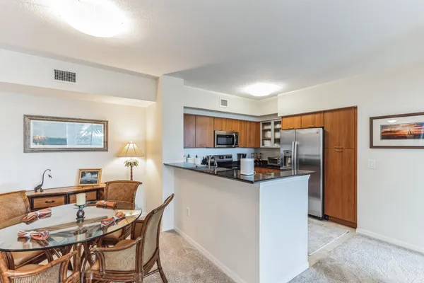 a kitchen with stainless steel appliances kitchen island granite countertop a dining table chairs and a refrigerator