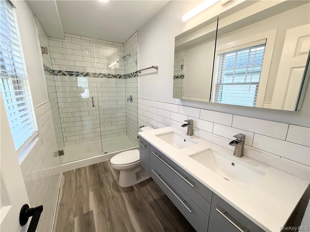 195 Park Avenue, Unit C West Harrison, NY 10604 - Photo 16 of 32 Full bath featuring double vanity, tile walls, dark wood-style floors, a stall shower, and plenty of natural light