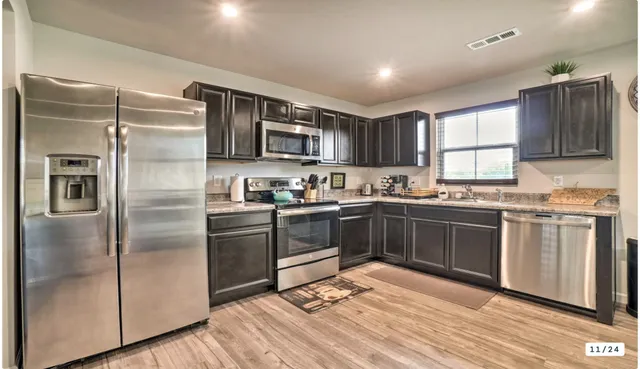 a kitchen with stainless steel appliances granite countertop a refrigerator a sink dishwasher a stove with wooden cabinets and floor