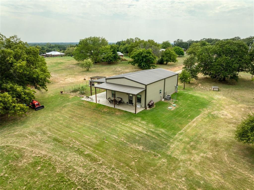 210 Spring Branch Trail North Springtown, TX 76082 - Photo 23 of 36 Metal-sided structure featuring a covered concrete patio, an expansive lawn, and mature trees