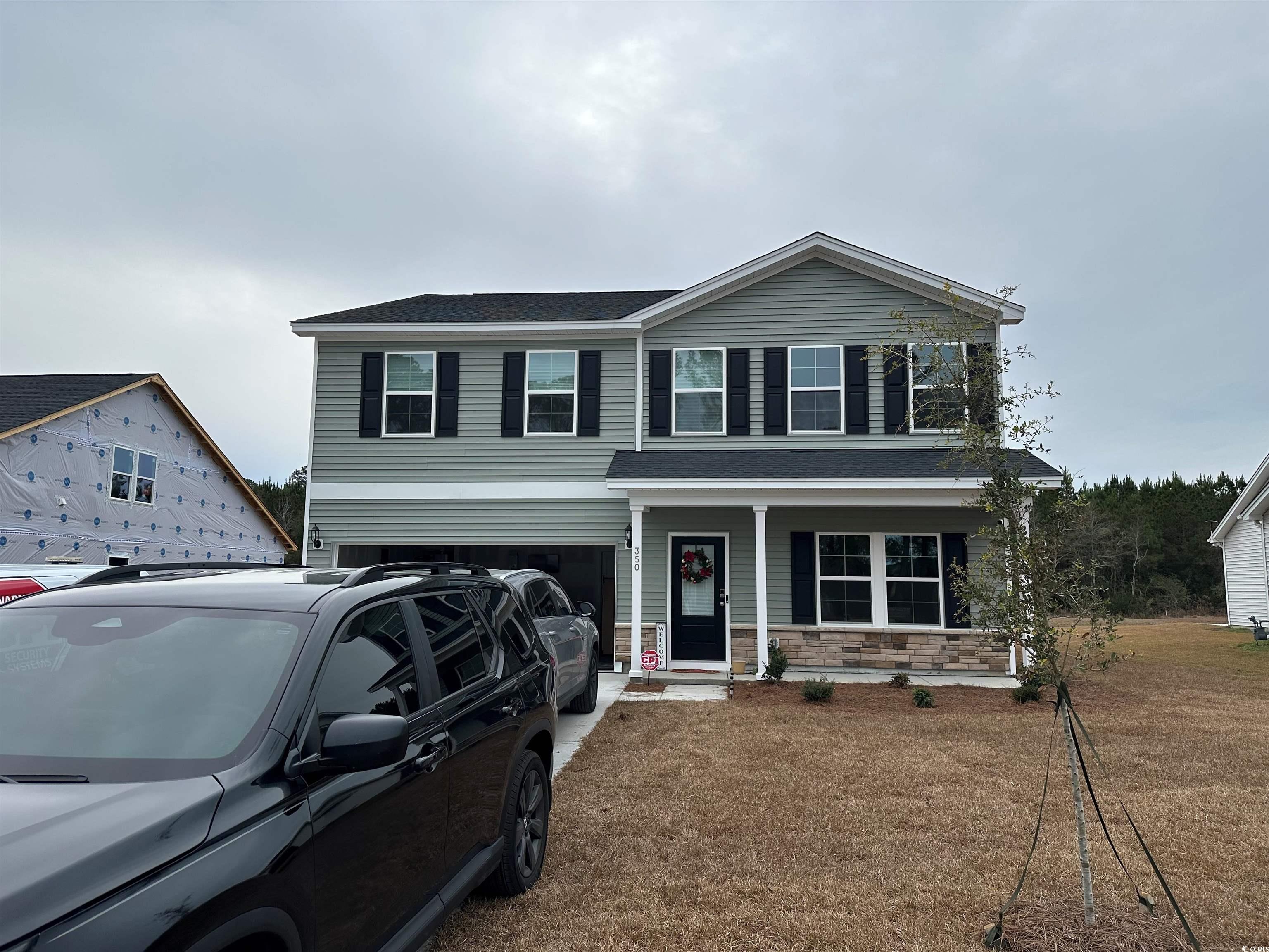Traditional home featuring covered porch, stone siding, roof with shingles, a garage, and a front yard