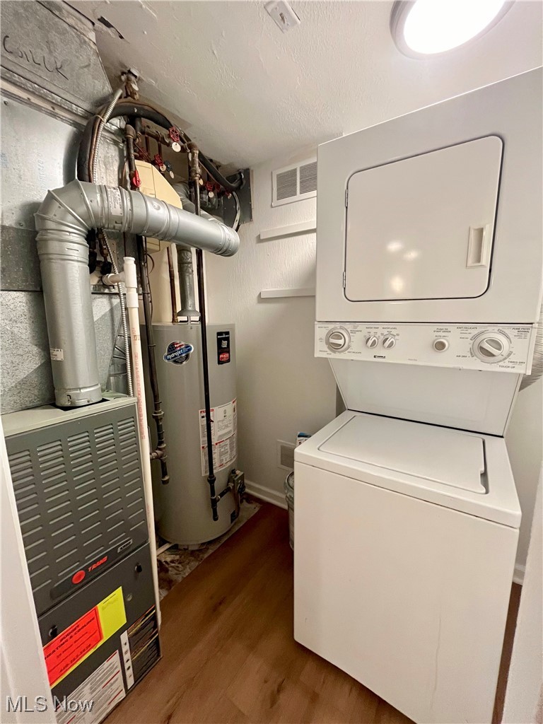22701 Center Ridge Road, Unit 201 Rocky River, OH 44116 - Photo 33 of 37 Clothes washing area with stacked washer / drying machine, dark hardwood / wood-style floors, a textured ceiling, and gas water heater