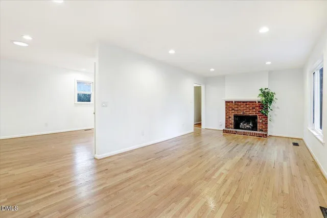 an empty room with wooden floor fireplace and windows