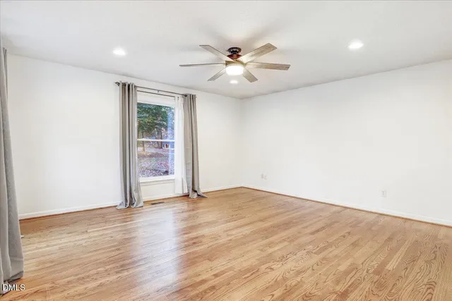 a view of an empty room with wooden floor and a ceiling fan
