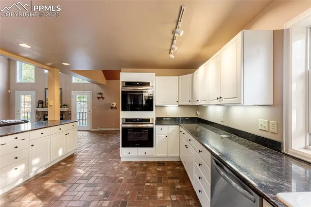 a large kitchen with stainless steel appliances granite countertop a large stove top oven a sink dishwasher and white cabinets with wooden floor