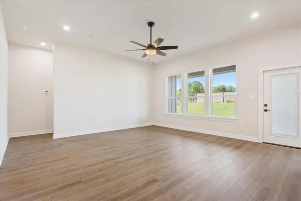 an empty room with wooden floor ceiling fan and windows