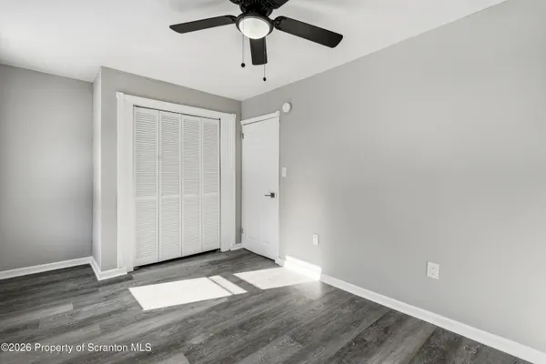 an empty room with wooden floor a ceiling fan and windows