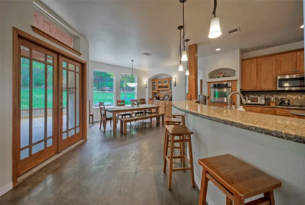 a kitchen with stainless steel appliances granite countertop a stove top oven a sink a dining table and chairs with wooden floor