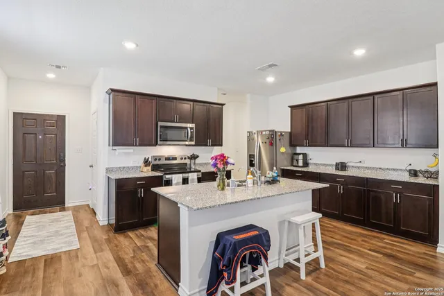 a kitchen with granite countertop a stove top oven a sink dishwasher a dining table and chairs with wooden floor