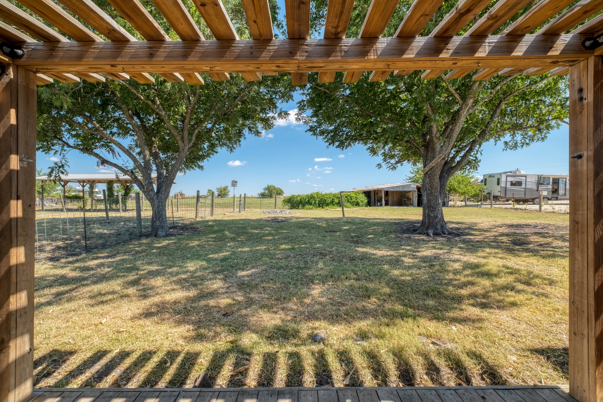 20960 Cameron Road Coupland, TX 78615 - Photo 17 of 21 Mature shade trees frame a peaceful pasture view from the shelter of a wooden pergola.