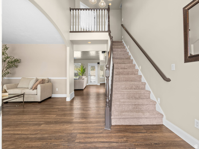 6849 North Black Powder Road Mountain Green, UT 84050 - Photo 2 of 43 Grand entryway featuring a carpeted staircase with a dark wood handrail and white balusters, wood-finish flooring, and light-toned walls with wainscoting