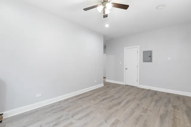 an empty room with a chandelier fan and wooden floor
