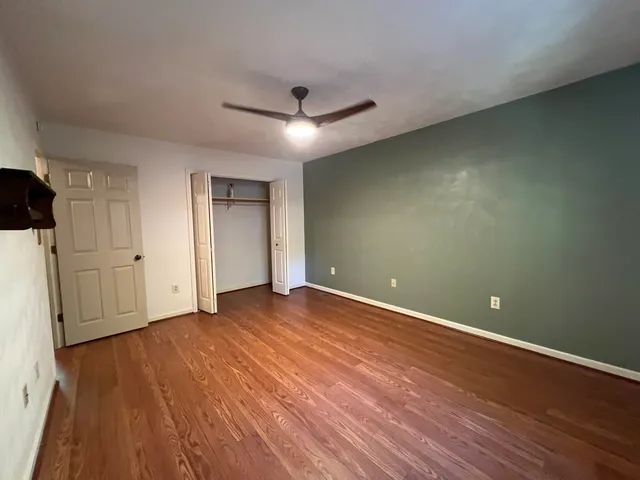 a view of an empty room with wooden floor and a ceiling fan