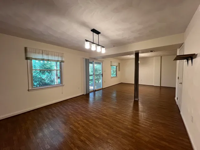an empty room with wooden floor chandelier and windows