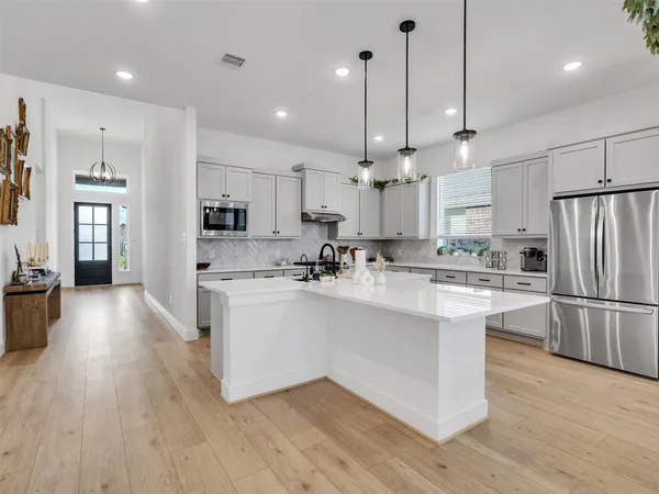 a kitchen with stainless steel appliances kitchen island granite countertop a refrigerator a stove a sink and a oven with wooden floor