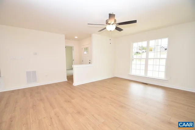 an empty room with wooden floor fan and windows