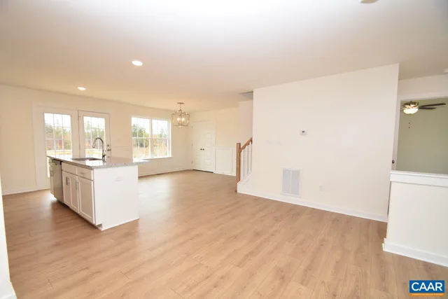 a view of an empty room and kitchen with wooden floor