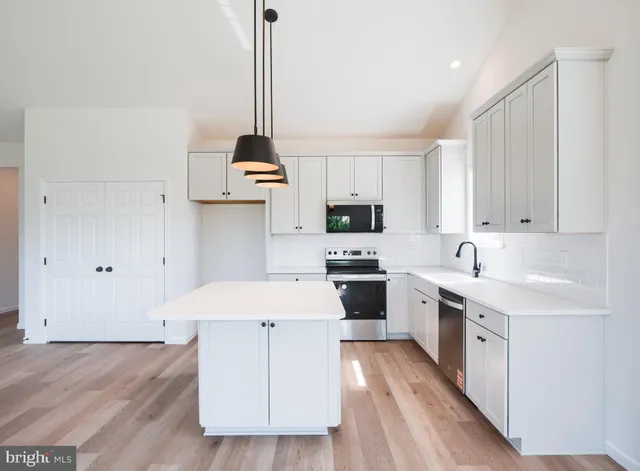 a large kitchen with kitchen island granite countertop a stove a sink and white cabinets with wooden floor