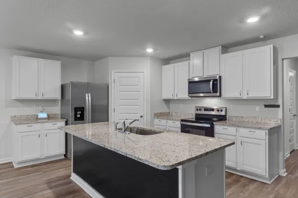 a kitchen with kitchen island granite countertop a sink dishwasher stove and white cabinets with wooden floor