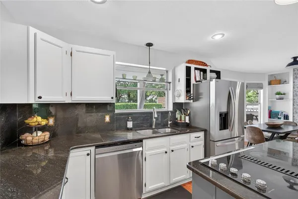 a kitchen with stainless steel appliances kitchen island granite countertop a refrigerator a stove a sink a dining table and chairs with wooden floor