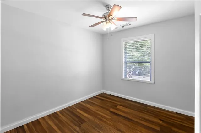 an empty room with wooden floor chandelier fan and windows