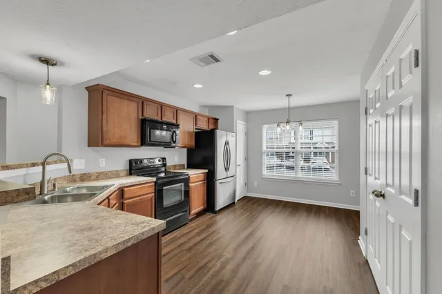 a kitchen with stainless steel appliances granite countertop wooden cabinets a refrigerator a sink a stove a microwave and wooden floors