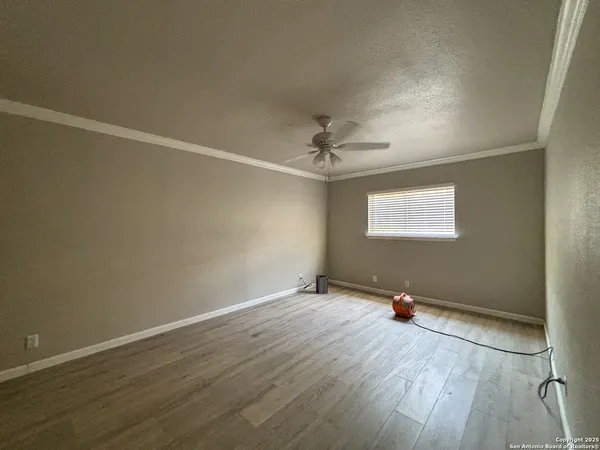 an empty room with wooden floor chandelier fan and windows