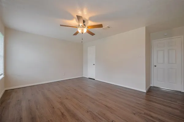 an empty room with wooden floor fan and windows